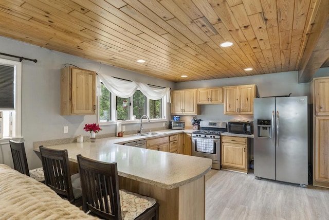 kitchen with stainless steel appliances, light countertops, light brown cabinets, a sink, and a peninsula