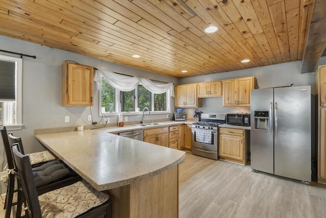 kitchen with light wood finished floors, a peninsula, stainless steel appliances, light brown cabinets, and a sink