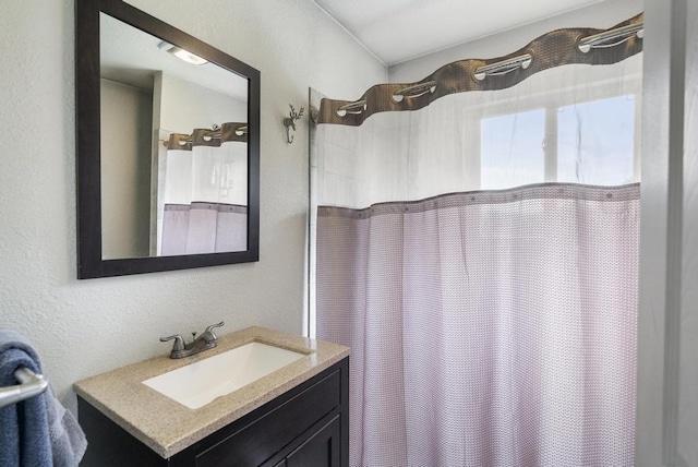 bathroom with a textured wall, curtained shower, and vanity