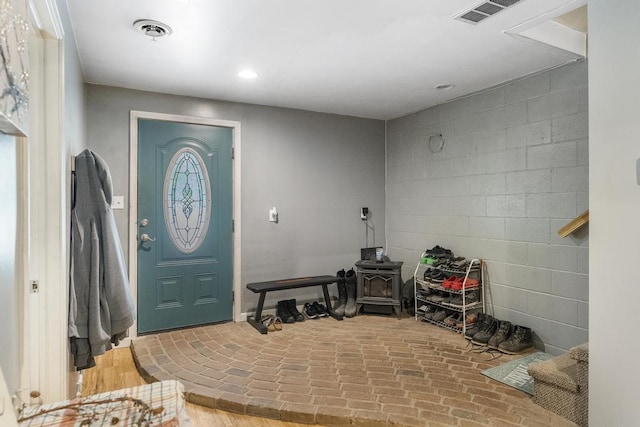 foyer entrance with a wood stove, brick floor, visible vents, and recessed lighting