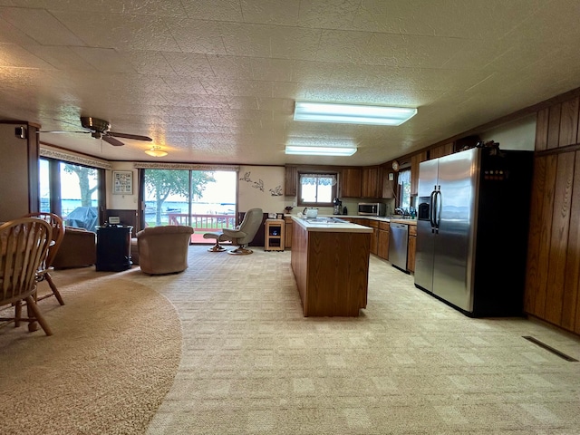 kitchen with dark brown cabinets, ceiling fan, light colored carpet, a kitchen island, and appliances with stainless steel finishes