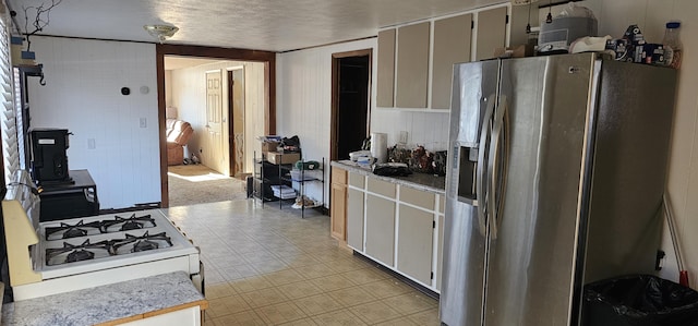 kitchen featuring stainless steel fridge, a textured ceiling, white cabinets, white gas stove, and wood walls