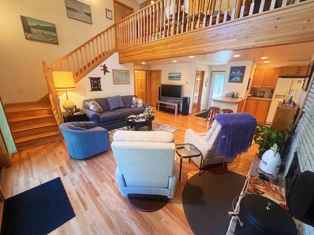 living area with light wood-style flooring, a high ceiling, and stairs