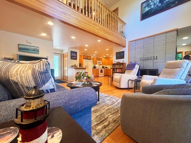 living room featuring a towering ceiling, light wood-style flooring, and recessed lighting