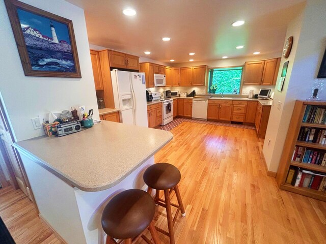 kitchen with white appliances, light wood-style flooring, a peninsula, light countertops, and recessed lighting