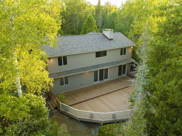 exterior space featuring roof with shingles, a chimney, and a wooded view