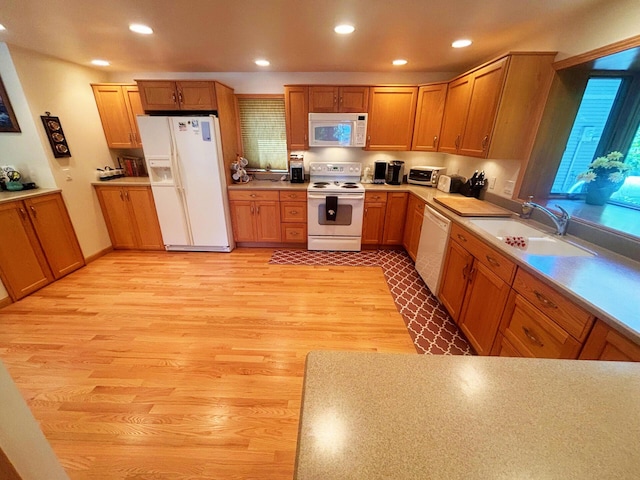 kitchen featuring recessed lighting, white appliances, a sink, light countertops, and light wood-type flooring