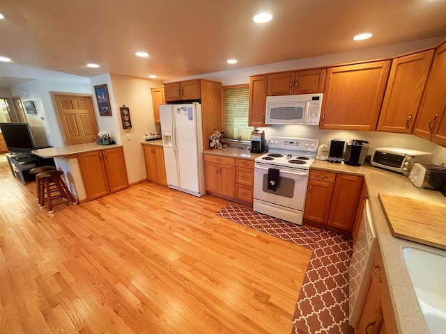 kitchen featuring a kitchen breakfast bar, white appliances, light wood-type flooring, and recessed lighting