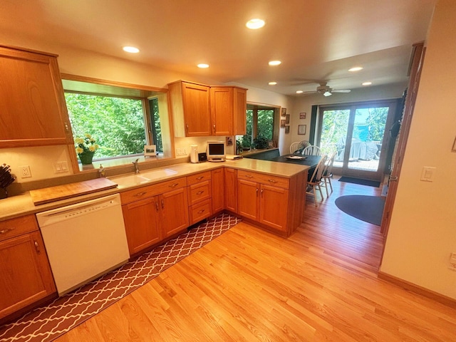 kitchen featuring light wood-style flooring, a peninsula, white dishwasher, light countertops, and a sink