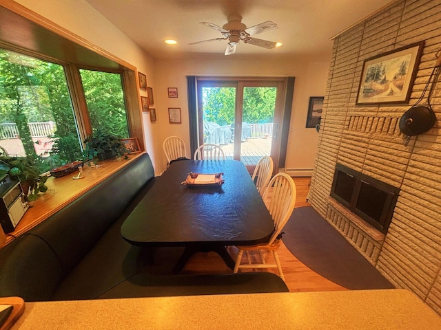 dining space featuring a fireplace, a baseboard radiator, recessed lighting, a ceiling fan, and wood finished floors