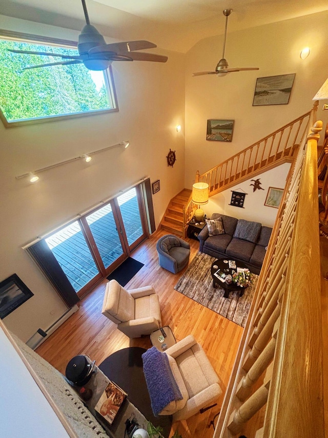 living area with ceiling fan, wood finished floors, stairs, and a towering ceiling