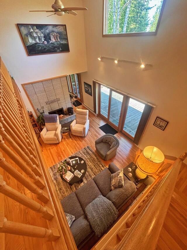 living area with a high ceiling, a ceiling fan, a fireplace, and wood finished floors