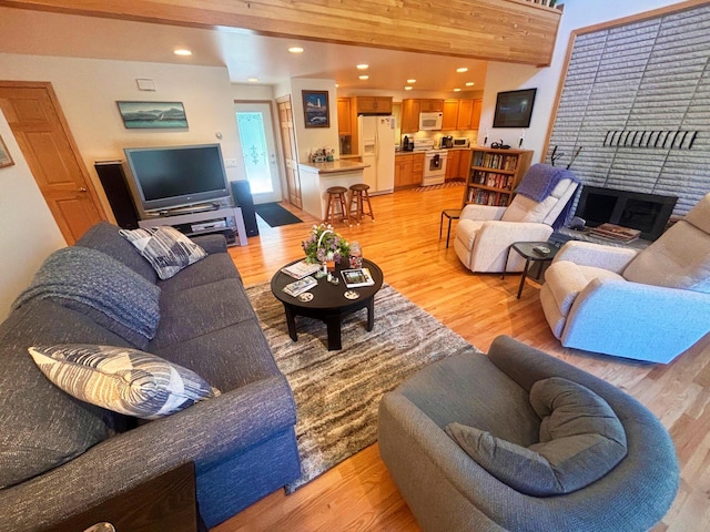 living room with recessed lighting, beam ceiling, a fireplace, and light wood finished floors