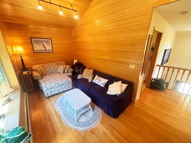 living room with rail lighting, vaulted ceiling, wooden walls, and wood finished floors