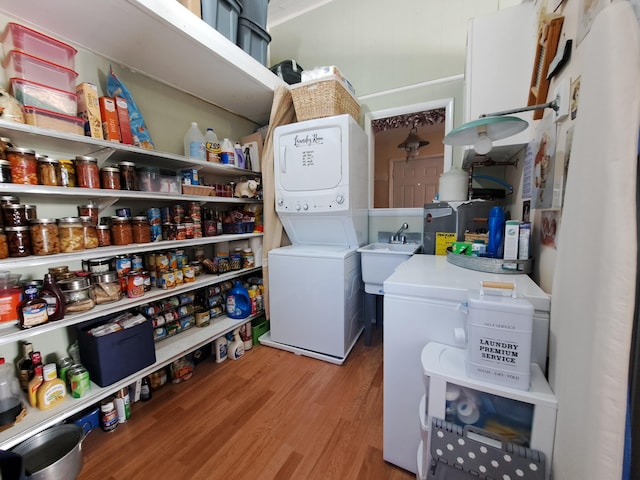 clothes washing area with stacked washer / drying machine, sink, and light wood-type flooring