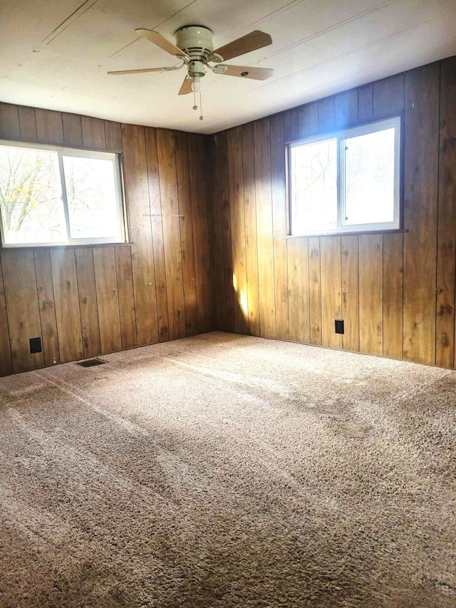 carpeted empty room featuring wood walls, ceiling fan, and a healthy amount of sunlight