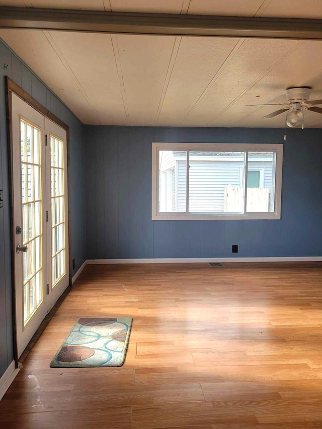 empty room featuring ceiling fan, plenty of natural light, wooden walls, and light wood-type flooring