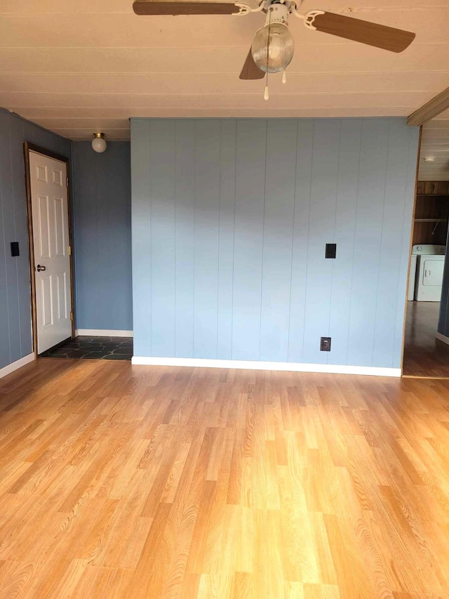 empty room featuring light hardwood / wood-style floors, ceiling fan, wooden walls, and washer / clothes dryer