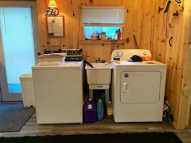 laundry area featuring wood walls, sink, wood-type flooring, and washer and clothes dryer