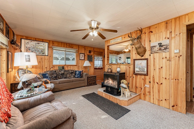 living room with a wood stove, wooden walls, carpet flooring, and ceiling fan