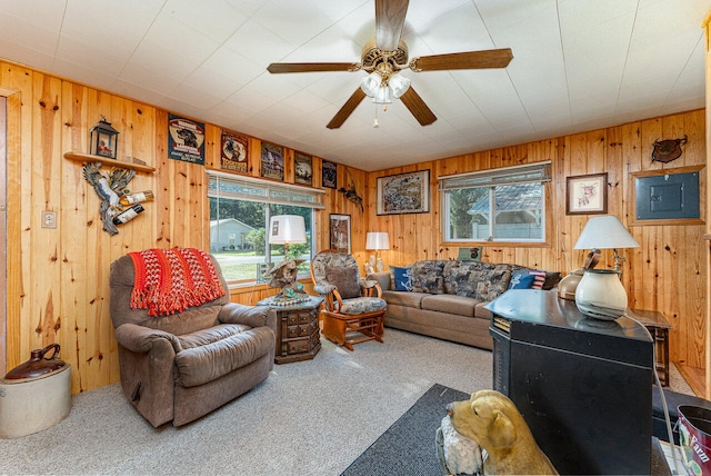 carpeted living room featuring ceiling fan, wood walls, and plenty of natural light