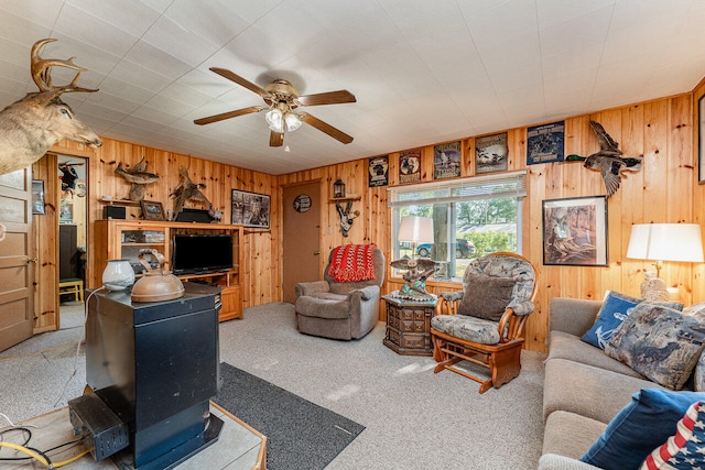 carpeted living room featuring ceiling fan, wood walls, and a wood stove