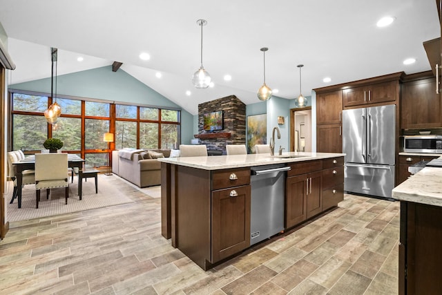 kitchen featuring appliances with stainless steel finishes, decorative light fixtures, sink, a kitchen island with sink, and light stone counters