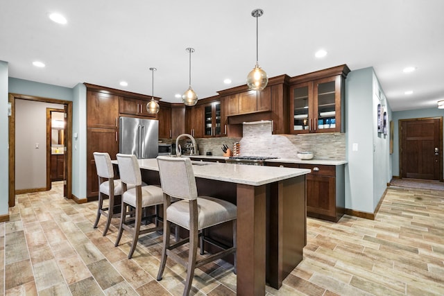 kitchen with sink, high end refrigerator, decorative light fixtures, a kitchen island with sink, and light hardwood / wood-style floors