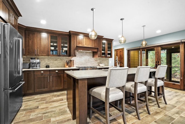 kitchen featuring high quality fridge, pendant lighting, tasteful backsplash, a center island, and dark brown cabinets