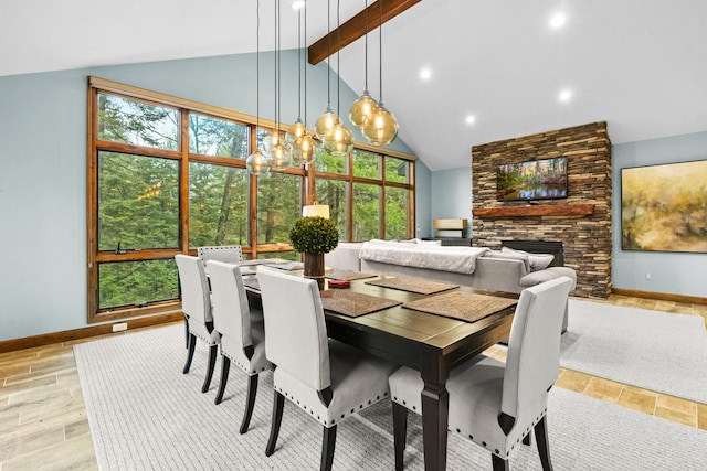 dining room featuring vaulted ceiling with beams, a stone fireplace, and plenty of natural light