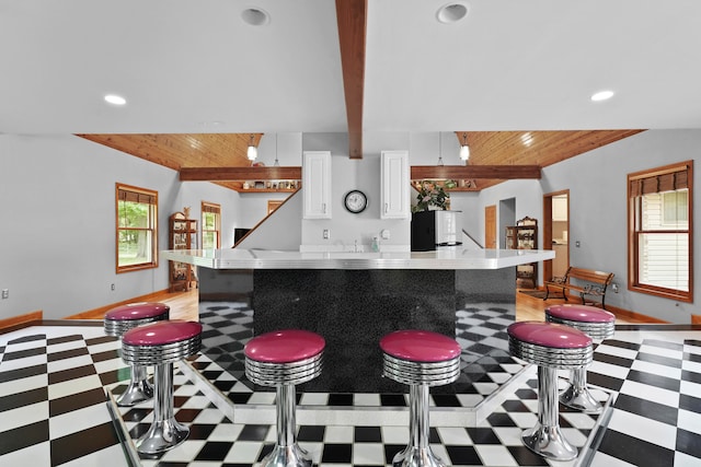 kitchen with fridge, white cabinets, light stone countertops, wooden ceiling, and a breakfast bar area