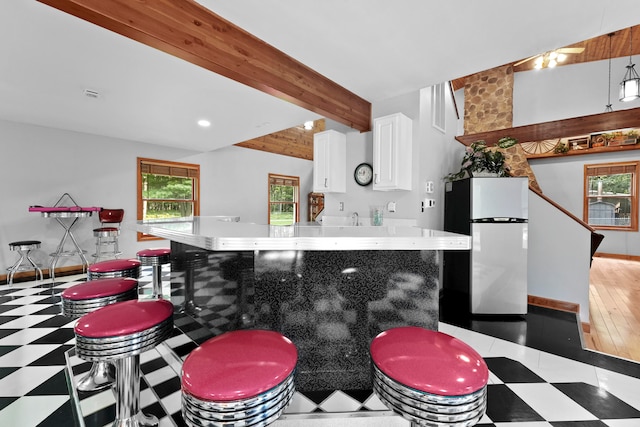 kitchen with beam ceiling, light hardwood / wood-style floors, white cabinets, and stainless steel refrigerator