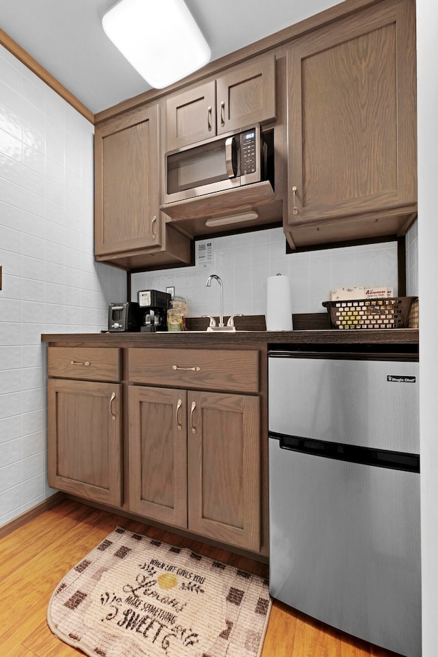 kitchen featuring dishwasher, stainless steel microwave, decorative backsplash, light hardwood / wood-style floors, and tile walls