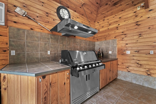 kitchen with dark tile patterned flooring, wooden ceiling, stove, wall chimney range hood, and lofted ceiling