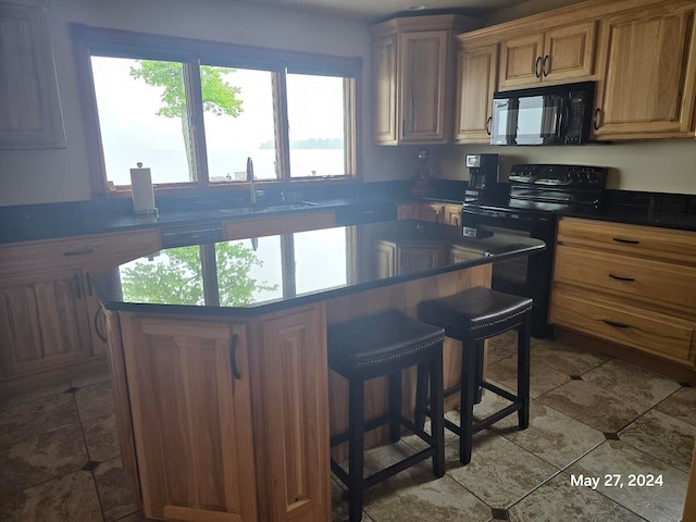 kitchen with sink, tile patterned flooring, black appliances, a kitchen breakfast bar, and a center island