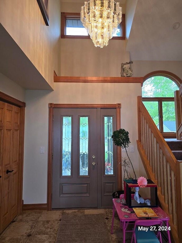 foyer entrance with tile patterned flooring, plenty of natural light, an inviting chandelier, and a towering ceiling