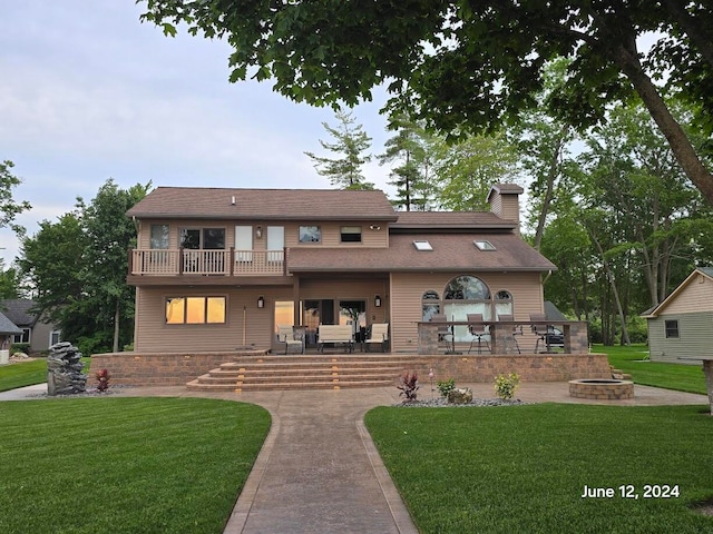 view of front facade with a patio, a balcony, a fire pit, and a front yard