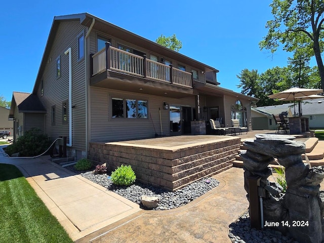 rear view of property with a balcony, a patio area, and a garage