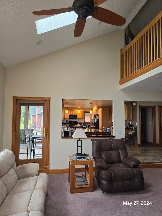 living room featuring high vaulted ceiling, a skylight, a textured ceiling, carpet flooring, and ceiling fan