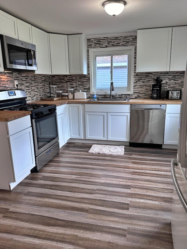 kitchen with tasteful backsplash, hardwood / wood-style floors, white cabinetry, sink, and stainless steel appliances