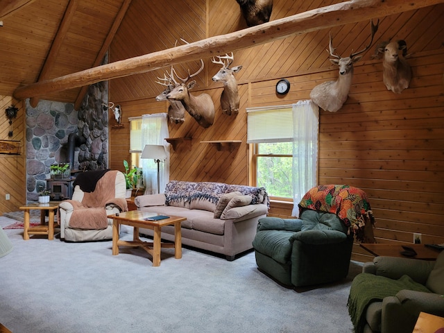 carpeted living room with wooden walls, beamed ceiling, and a wood stove