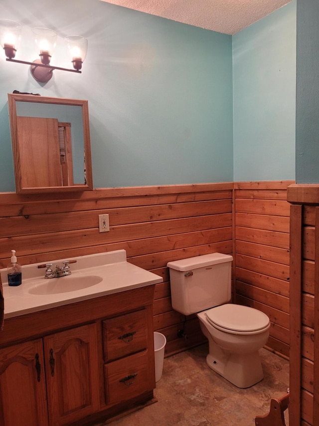 bathroom featuring wooden walls, toilet, a textured ceiling, and vanity