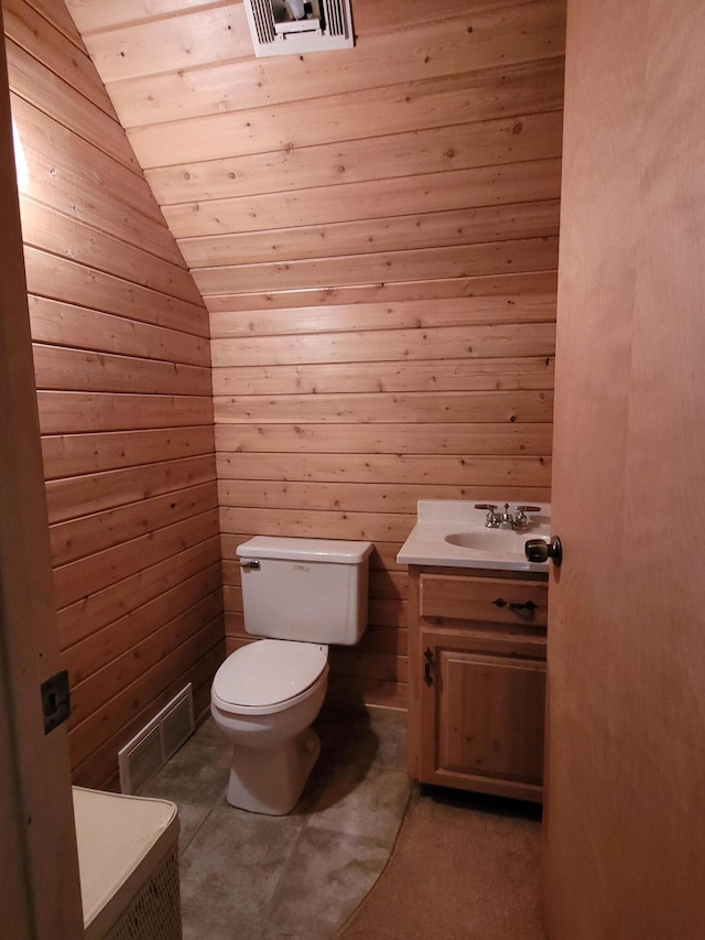 bathroom featuring toilet, lofted ceiling, wooden walls, and vanity