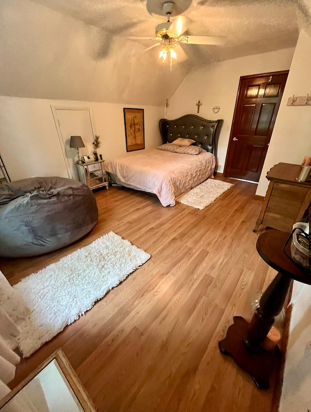 bedroom featuring ceiling fan, hardwood / wood-style floors, a textured ceiling, and lofted ceiling