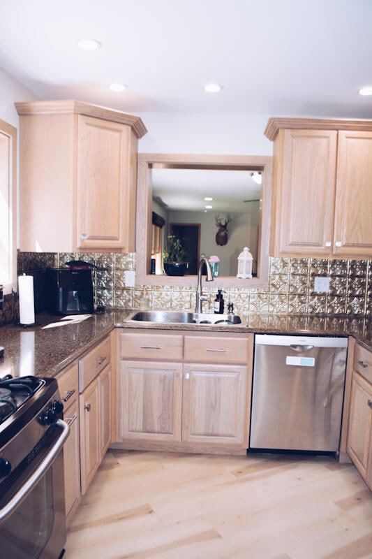 kitchen with light brown cabinets, sink, stainless steel appliances, light hardwood / wood-style floors, and decorative backsplash