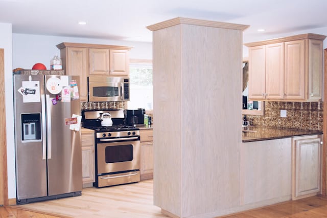 kitchen with light brown cabinets, appliances with stainless steel finishes, light wood-type flooring, and dark stone counters