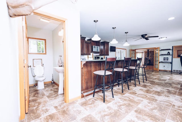 kitchen featuring a kitchen breakfast bar, kitchen peninsula, dark brown cabinets, ceiling fan, and decorative light fixtures