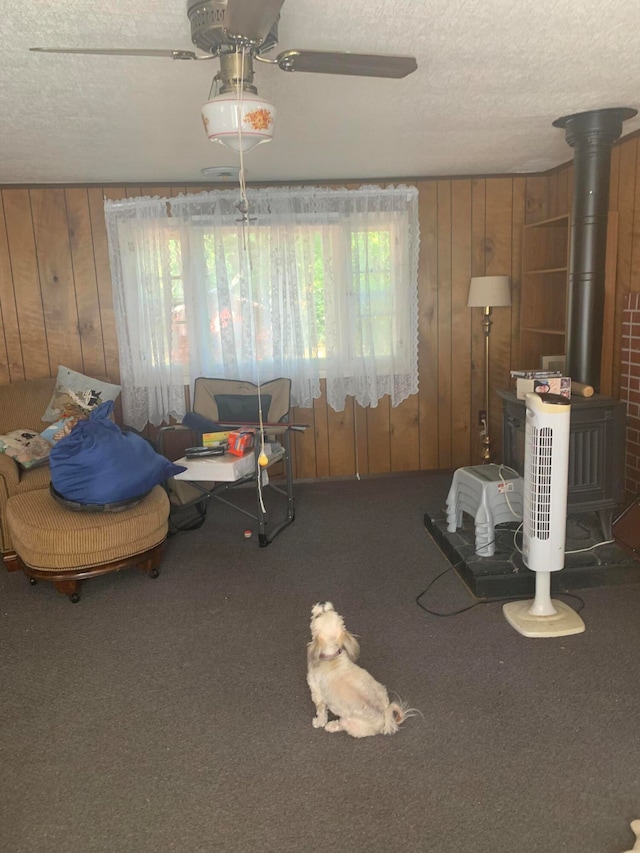 interior space featuring ceiling fan, a textured ceiling, wood walls, and a wood stove