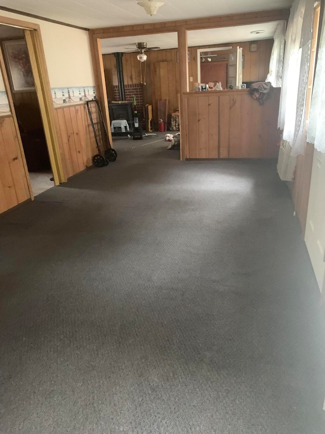 interior space with ceiling fan, wooden walls, carpet flooring, and a wood stove