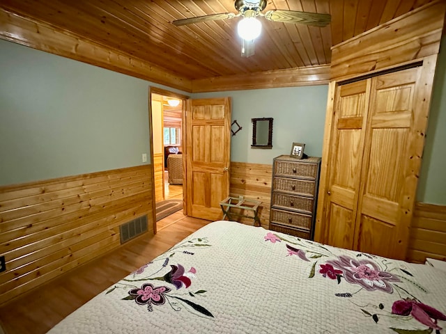 bedroom with wooden walls, ceiling fan, a closet, wooden ceiling, and light hardwood / wood-style floors